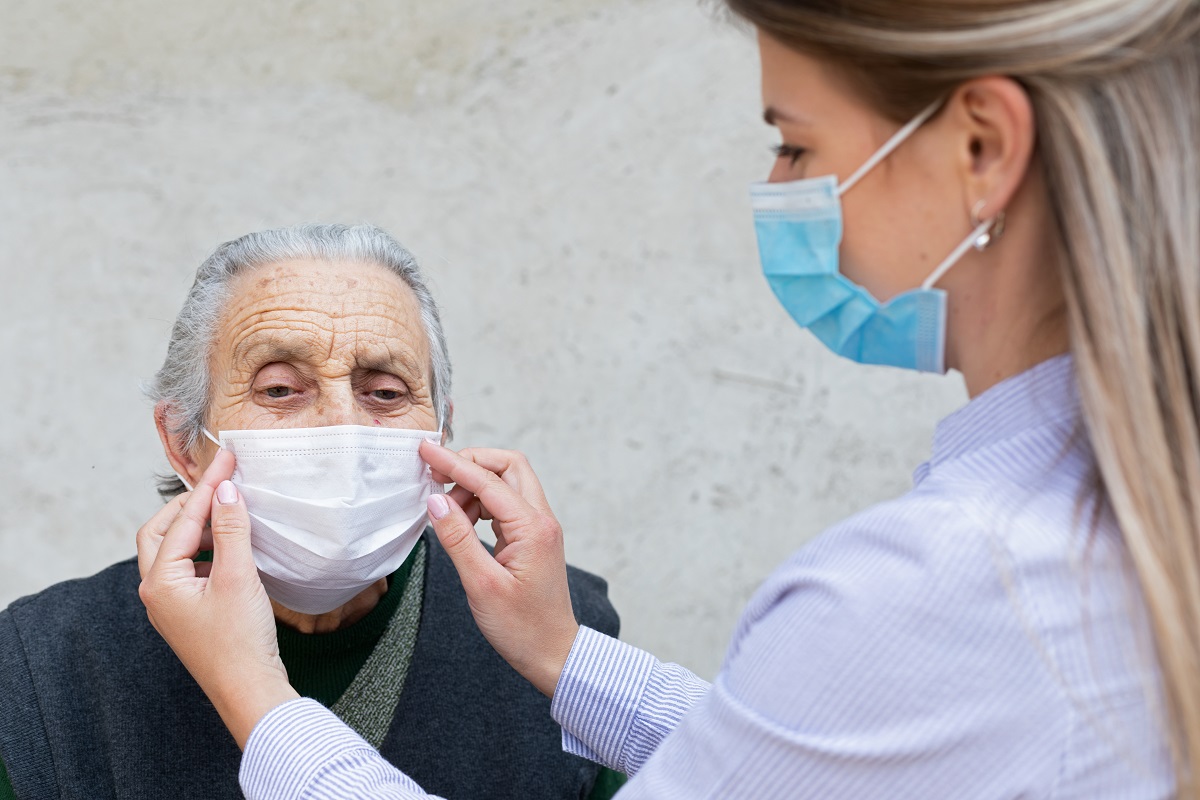 A personal care worker helps an older person put on a mask.