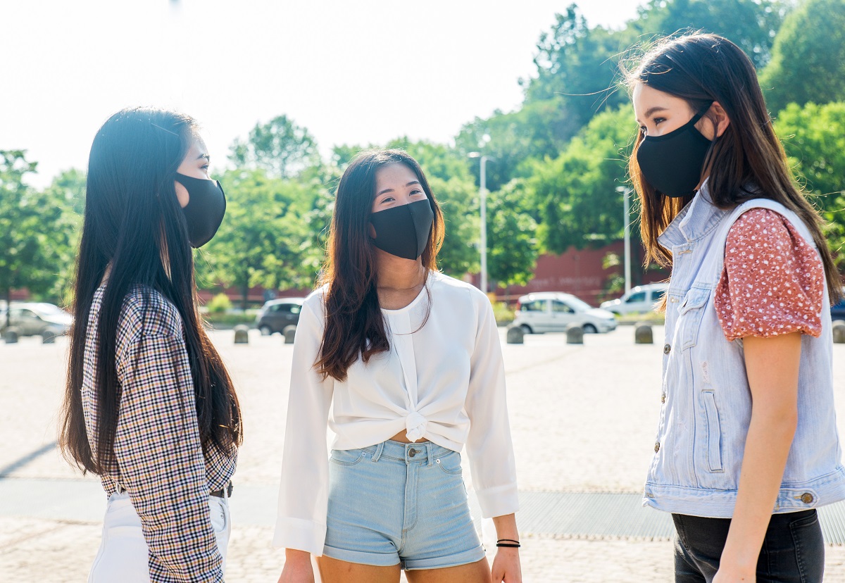 Three teenage girls with long brown hair stand near each other, wearing black face masks.