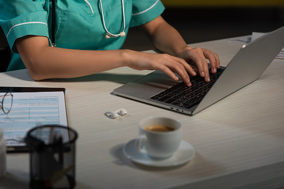 Image of a nurse's torso and hands typing on a laptop at a desk.