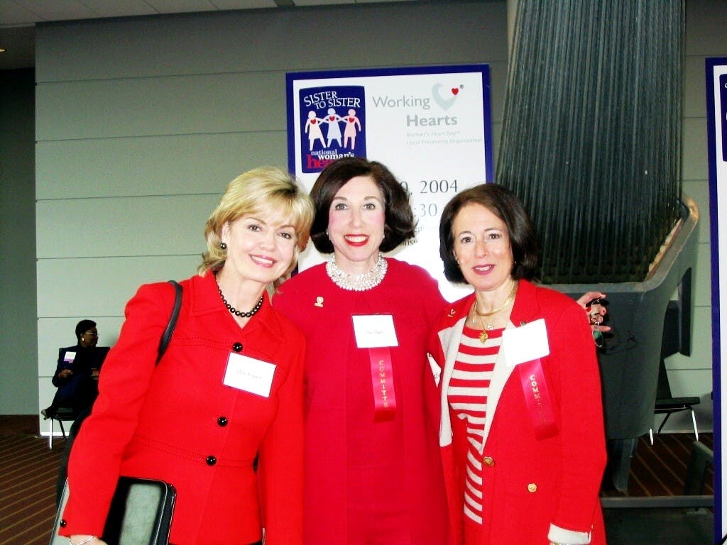 Three women in red in front of a sign that says “Working Hearts.”