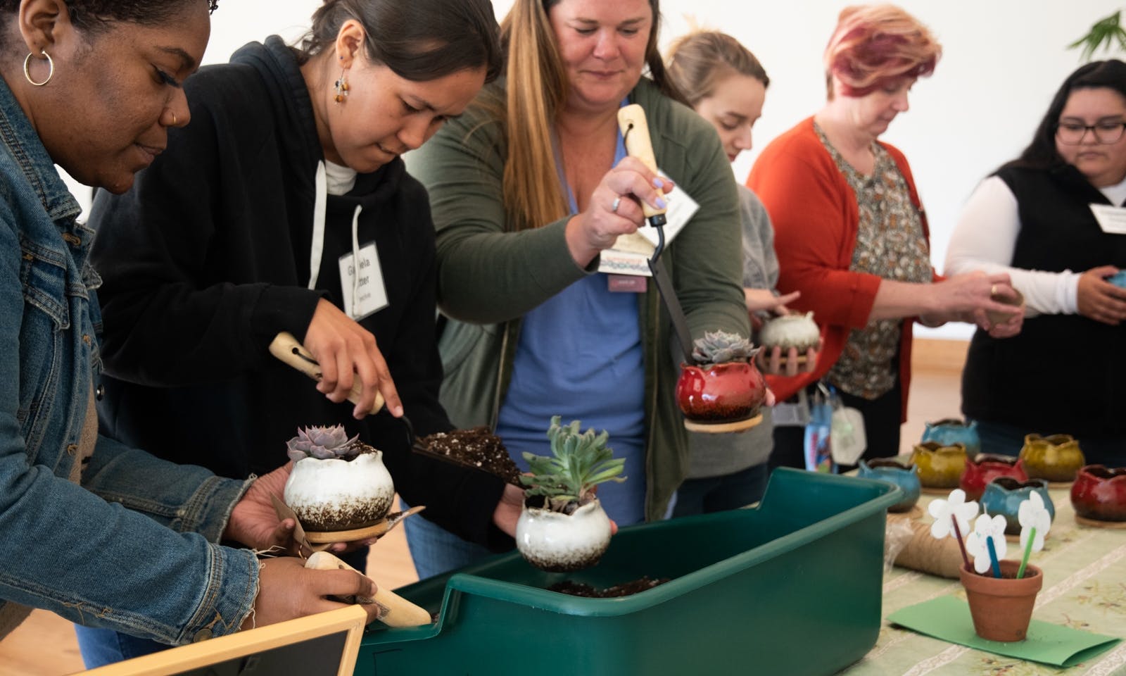 Six women planting succulents in small pots.