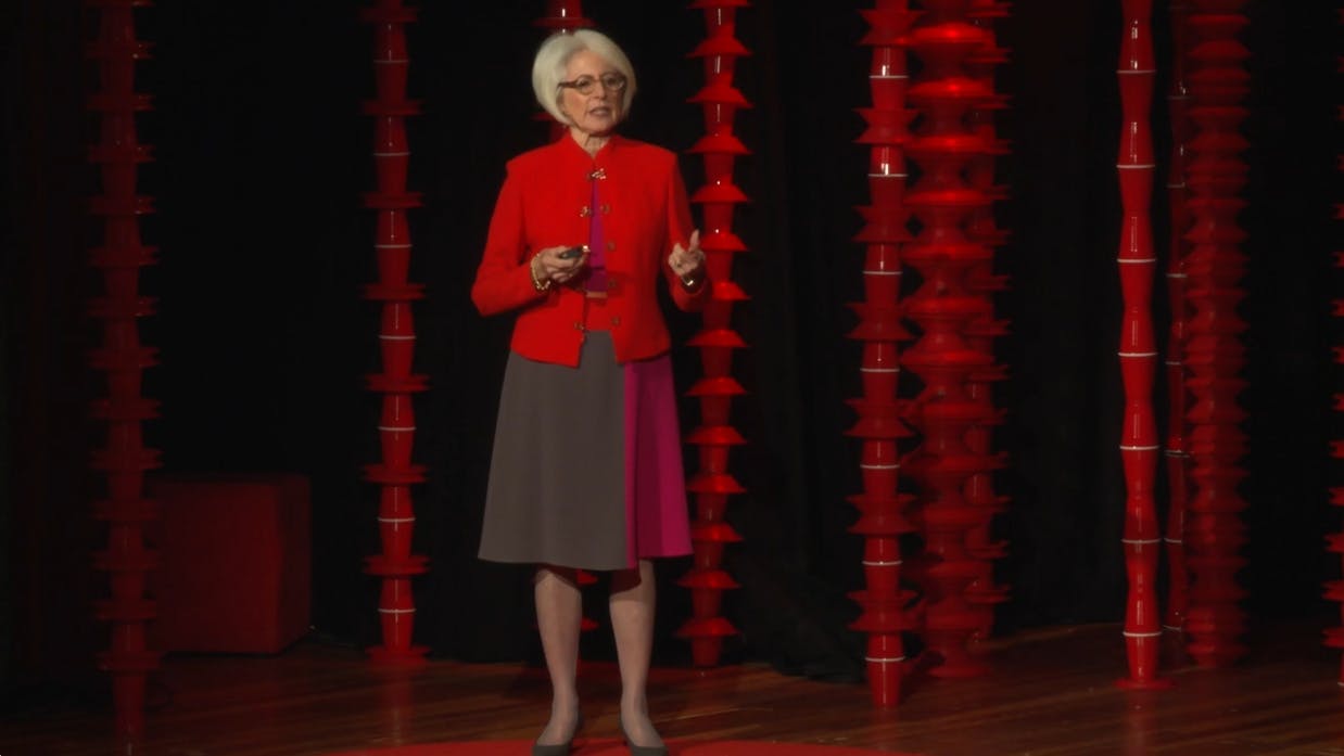 A woman in a red sweater presenting on a stage.